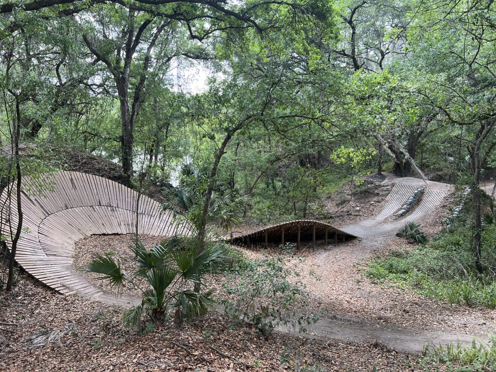 Twisting mountain bike course comprised of wood slats and dirt in a lush Florida forest.
