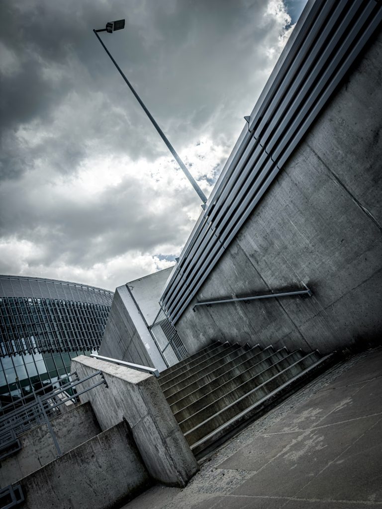 Image of a modernist style scene featuring a set of concrete stairs against a minimalist concrete wall. The stairs and wall showcase clean lines and geometric patterns, embodying the simplicity and functional aesthetics of modern architecture