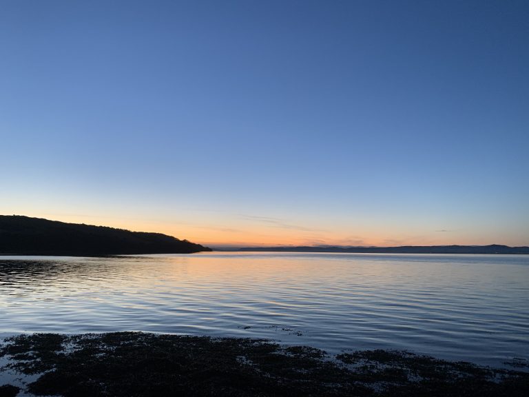 A late evening orange sunset in a blue sky looking out over Wormit Bay on the River Tay in Newport, Scotland.