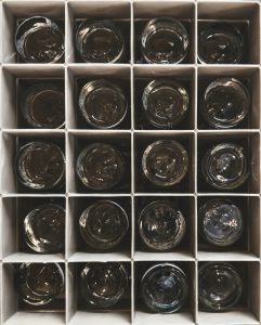 Overhead view of a box filled with identical glasses. Each glass has been neatly arranged, their uniformity creating a pattern of clear surfaces against the contrasting backdrop of the box.