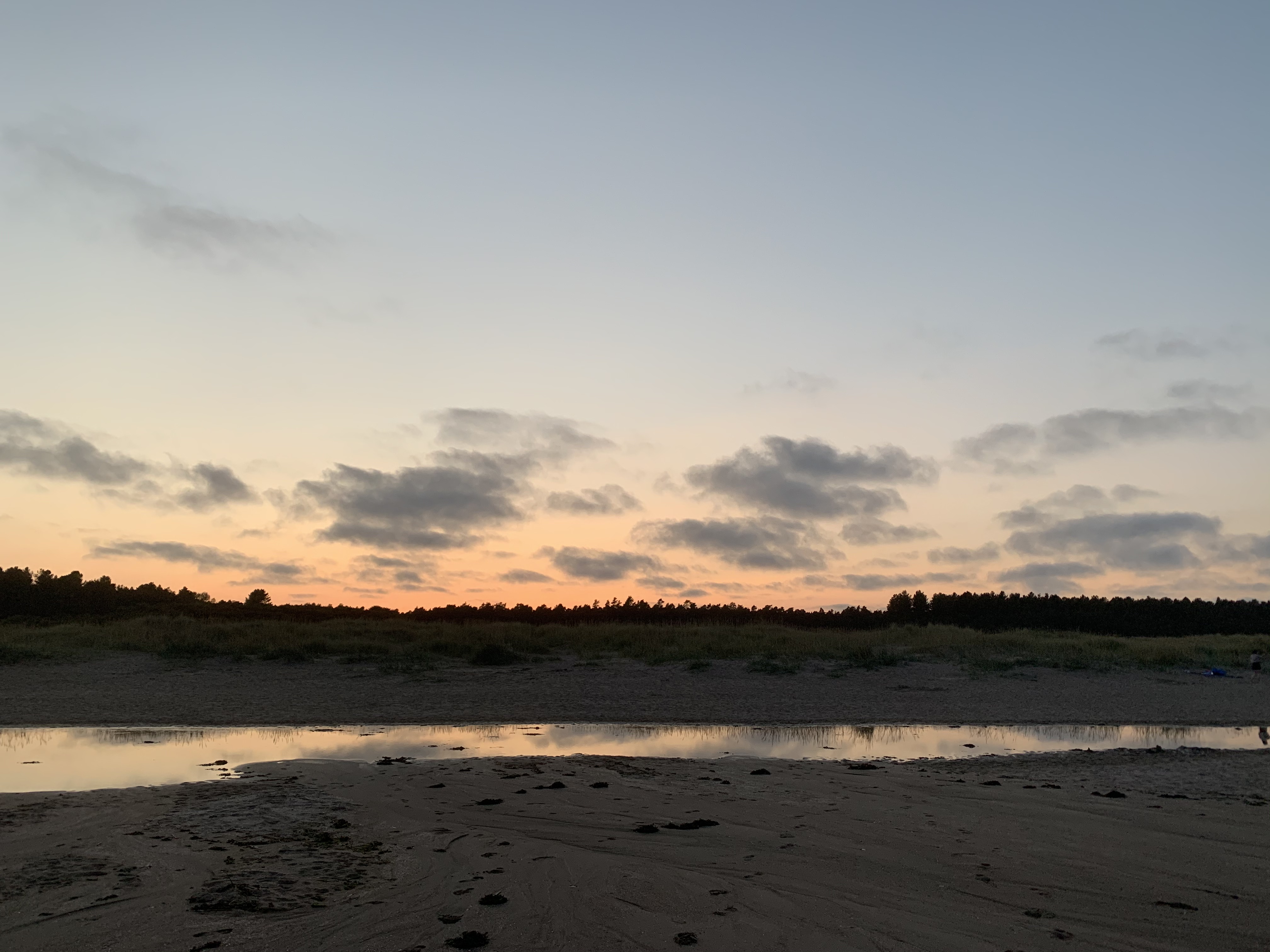 A late evening sunset view with clouds above treetops with a reflection in the water at Tentsmuir beach, ?Tayport?, ?Scotland?.