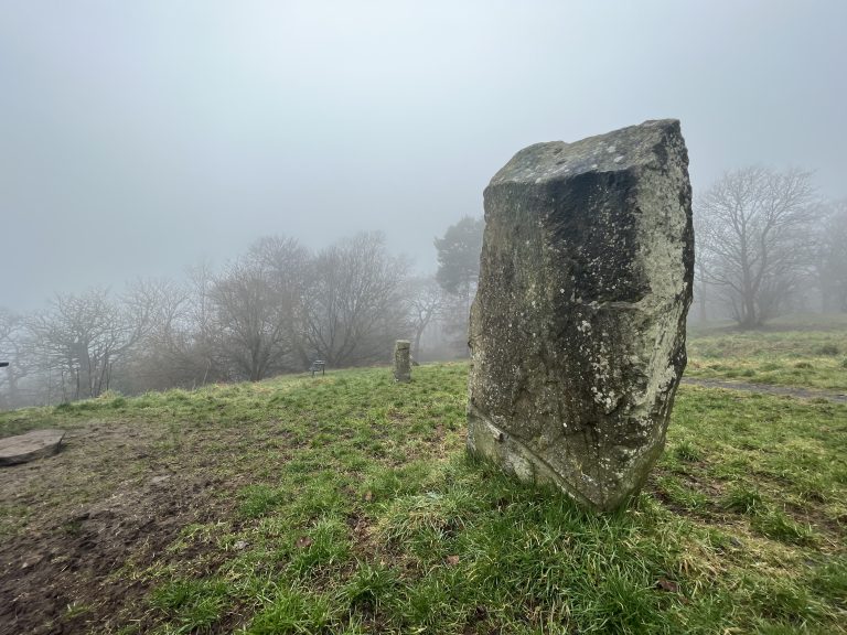 Standing stone situated amongst the grass with trees in the background on a foggy Balgay Hill in Dundee Scotland.