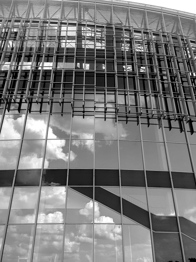 A view from the outside of a modern building that stands out with its minimalist style and simple, yet elegant form. The dominant material used in construction is glass, which provides the building with space and allows plenty of natural light into the interior. The photo showcases the impressive and modern character of the building.