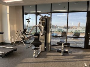 Bench press machine in a small gym with glass walls on the roof of a building. Grand Rapids Michigan visible outside.