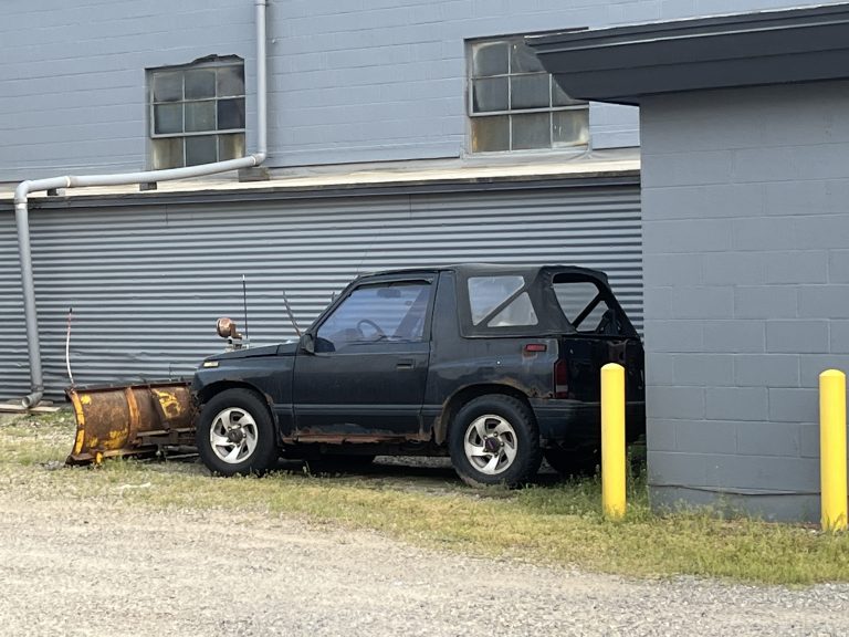 A vastly undersized Suzuki vehicle mounted with a plow blade.