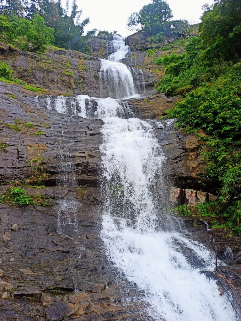 Mountain waterfall cascading down the mountain, surrounded by dense vegetation.