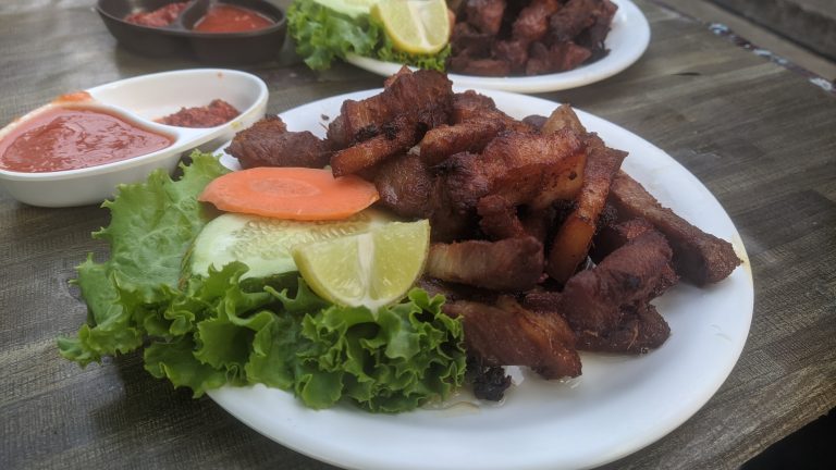 Pork sekuwa. Plate of fried pork strips next to some lettuce and citrus, a small bowl of sauce next to it.