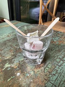 Turkish Delight dessert served in Athens, Greece at a little bistro downtown. Small glass on a rough table with candy in the bottom and two wooden sticks to eat with.