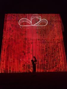 A person holding a child in silhouette in front of a large gift made of red lights.