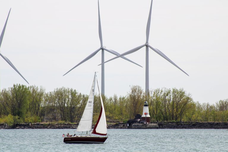 A sailboat passes a lighthouse and wind turbines as it enters Lake Erie at Buffalo, New York.