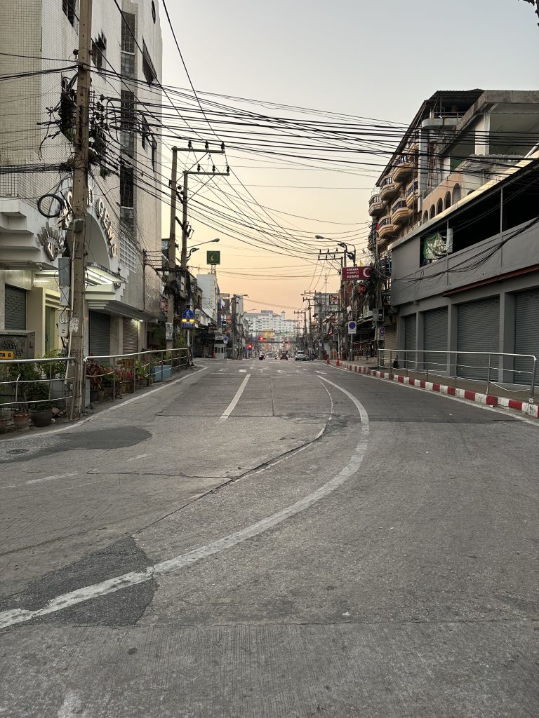 Pattaya city road.? Looking down a long empty street, many power lines crossing the street overhead, buildings on either side.