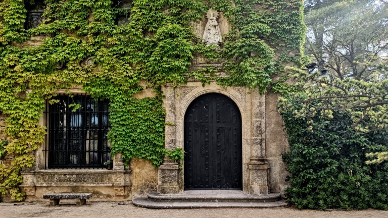 Fa?ade of the old stone building with an archway entrance. The walls are covered in ivy. There is a stone bench in front of the building, as well as a dormer window on one side. Finca Torrefiel, Fontanars dels Alforins, Valencia Spain.