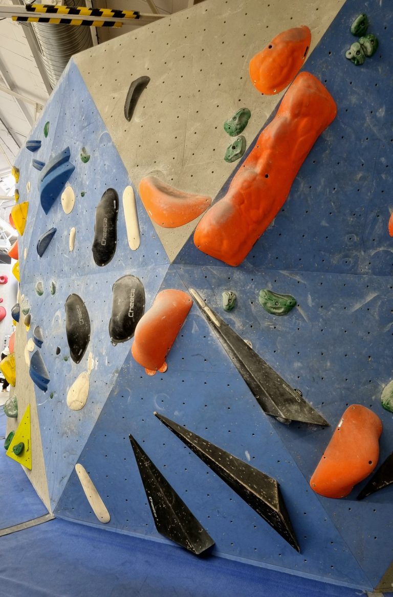 An indoor bouldering wall with a lot of colorful plastic rock holds for climbing.