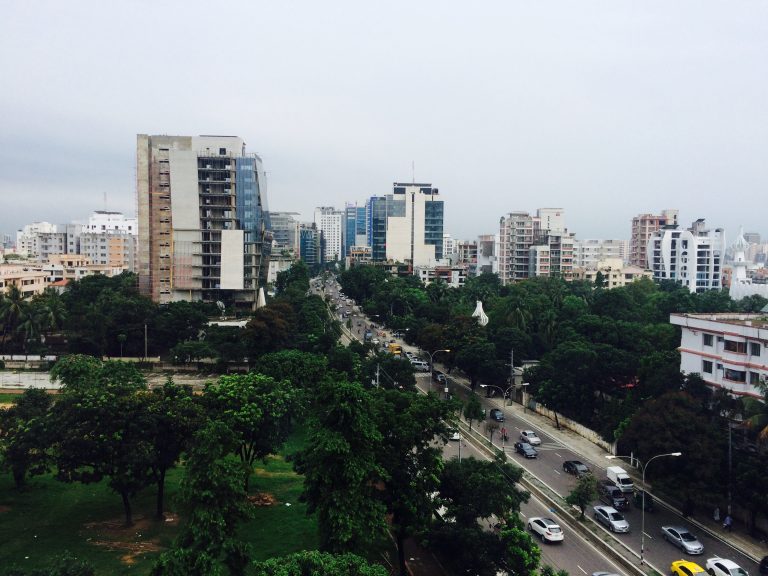 Traffic drives along a road through a busy city.