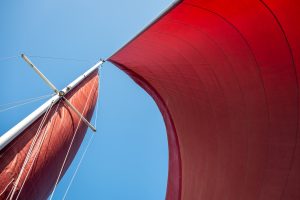 Mast and red sails photographed upwards from the deck of a sail boat.
