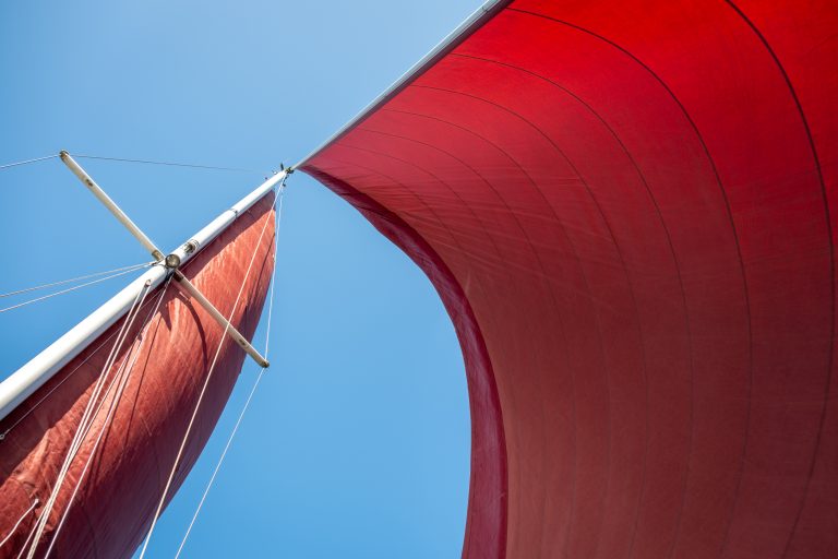 Mast and red sails photographed upwards from the deck of a sail boat.