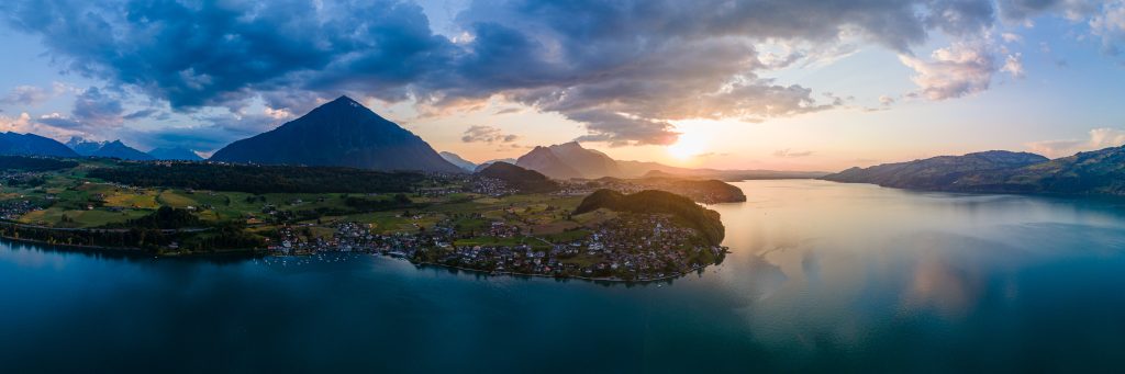 Aerial (drone) view of mountains and a sunset over the villages on the shore of a large lake in Switzerland.