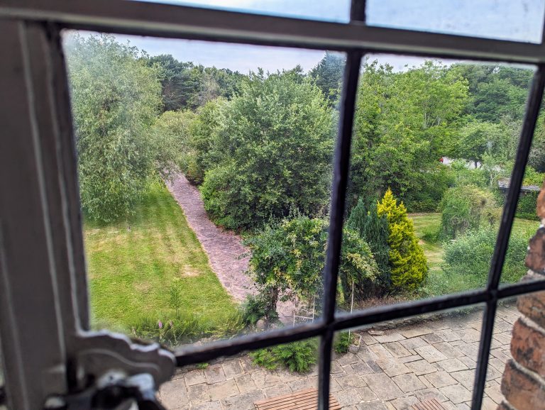 The view of a garden outside one of the Heskin Hall windows, an old manor house in North England. The photo includes some of the old metal window frame and glass.