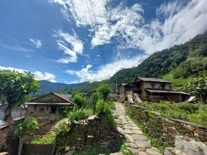 A serene Gurung village in the western part of Nepal. Stone topped pavement surrounded by stone roofed houses under the clear sky with partial clouds and hilly jungle above the houses.
