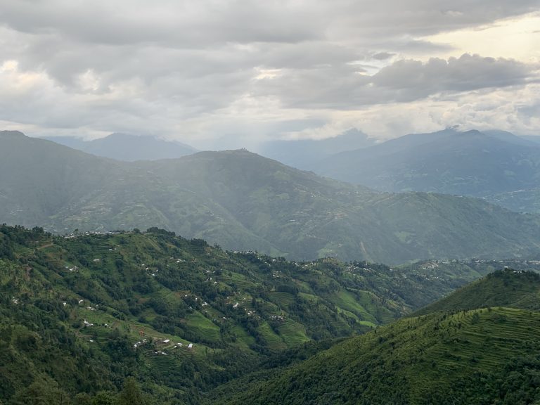 A village in nepal with some houses in the background and a sky starting to cloud over.