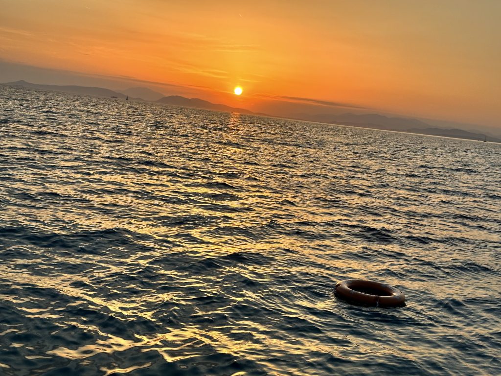 Sunset over the Aegean Sea. A life preserver is floating just to the right in the frame.