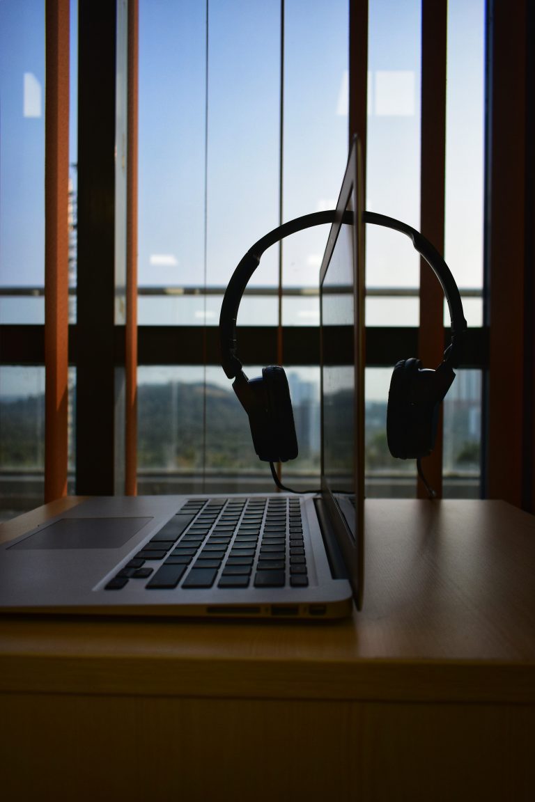 A work desk in a city office with a macbook air and a headset hanging over the screen.