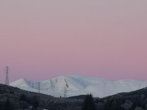 Snow on the mountain, pink sky, pylons and wind turbines