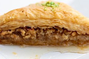 Baklava close up showing layers of filo pastry, filled with chopped nuts and covered in honey with the honey pooling at the bottom
