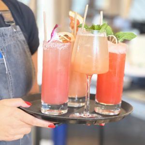 four fruity cocktails on a tray held by a waiter with bright red nail polish