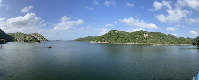 A lake with greenery hills and a clear sky with clouds.