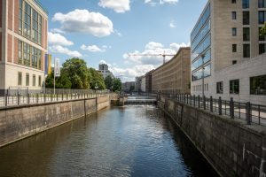 View from the Schleusenbrücke in Berlin, featuring several large buildings along a canal, as well as a sluice-gate.
