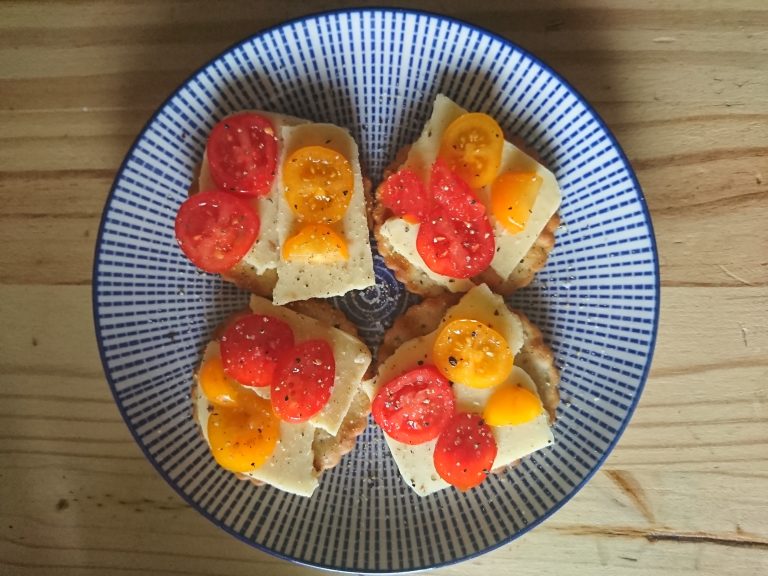 Seasoned tomato slices on cheese on crackers.? Four crackers arranged on a plate.