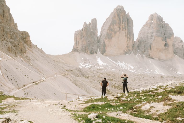 Two people taking photos with a view of the trail and three mountains..