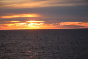 Sunset over the Baltic Sea with the sun partly hidden in the clouds and reflecting in the sea.
