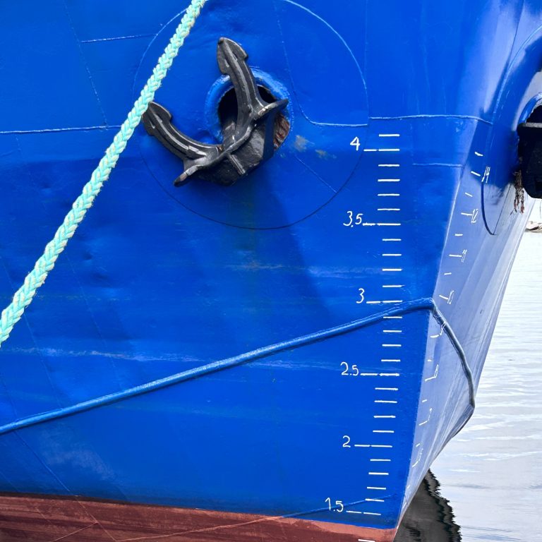 Close up of a blue ship’s plimsoll lines (reference marks located on a ship’s hull that indicates the maximum depth to which the vessel may be safely immersed when loaded with cargo). The anchor and a green rope is also visible.