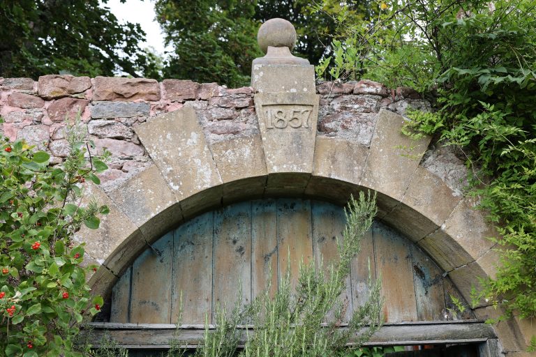 Old stone arch built in 1857, overgrown with foliage, a take over of nature