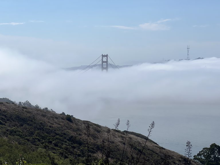 The top of the San Fransisco bridge visible in the distance above a layer of fog.