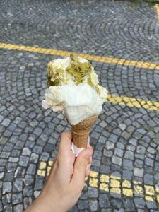 Ricotta Pistacchio and Farina Bona Ice Cream held in a cone with a backdrop of grey stone road and yellow street markings.
