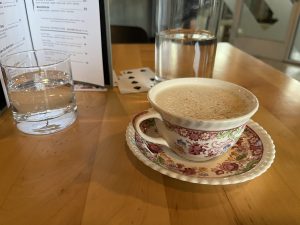 A tea-based whiskey cocktail in a vintage teacup on matching saucer. Surrounded by a menu and water glasses.