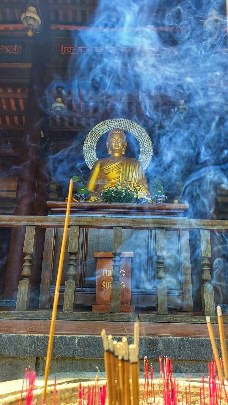 Buddha in background with incense sticks and incense smoke