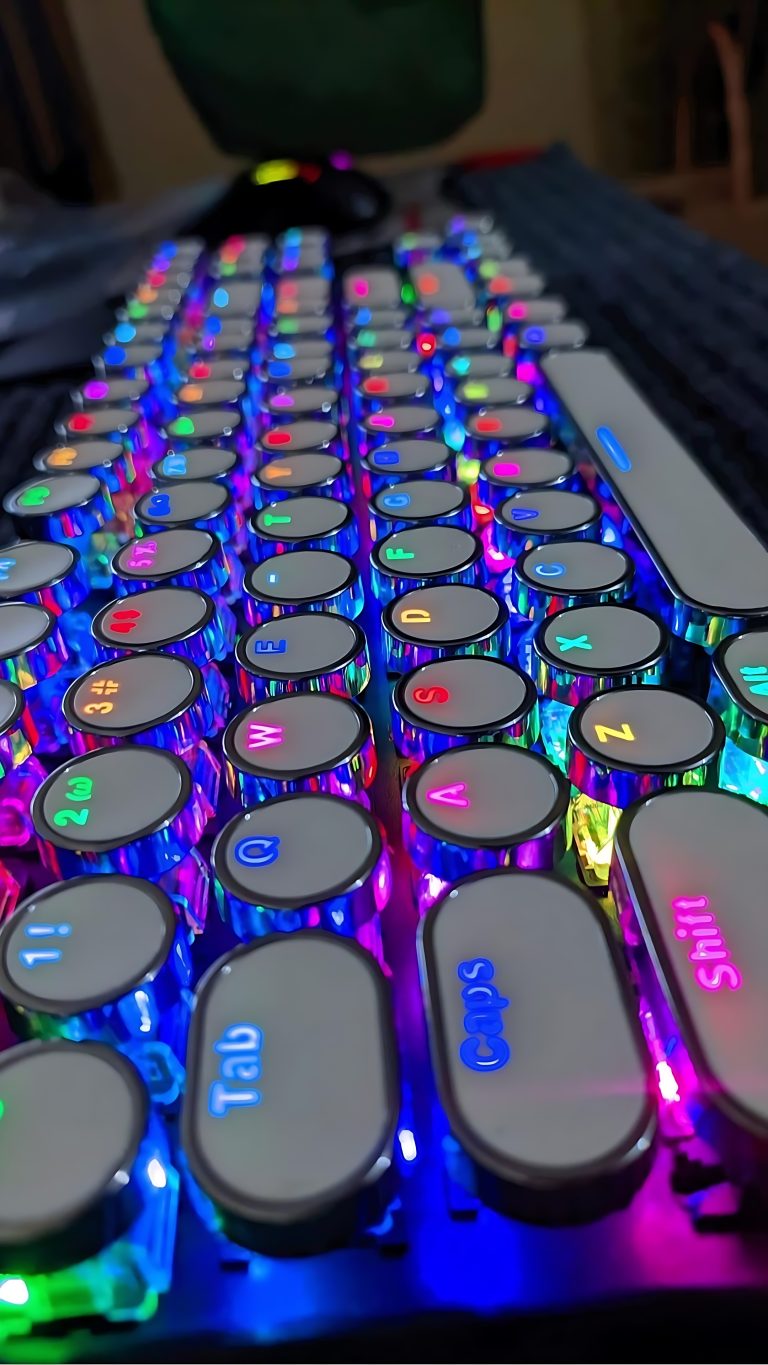 Closeup of a computer keyboard.  Each key is round, and has mirrored reflective sides. Each letter is backlit in a bright neon color.