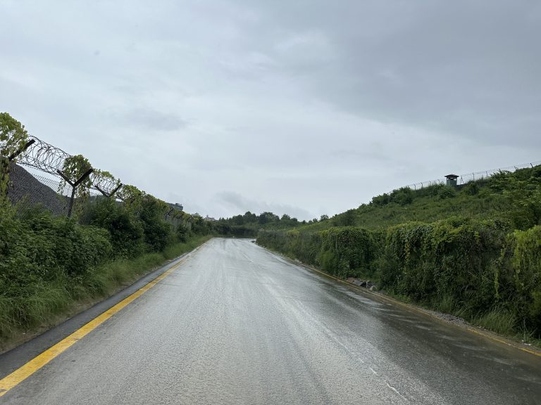 Wet Road, Greenery, Small Hill and Wired Fence on the Side, Cloudy Sky During Rainfall