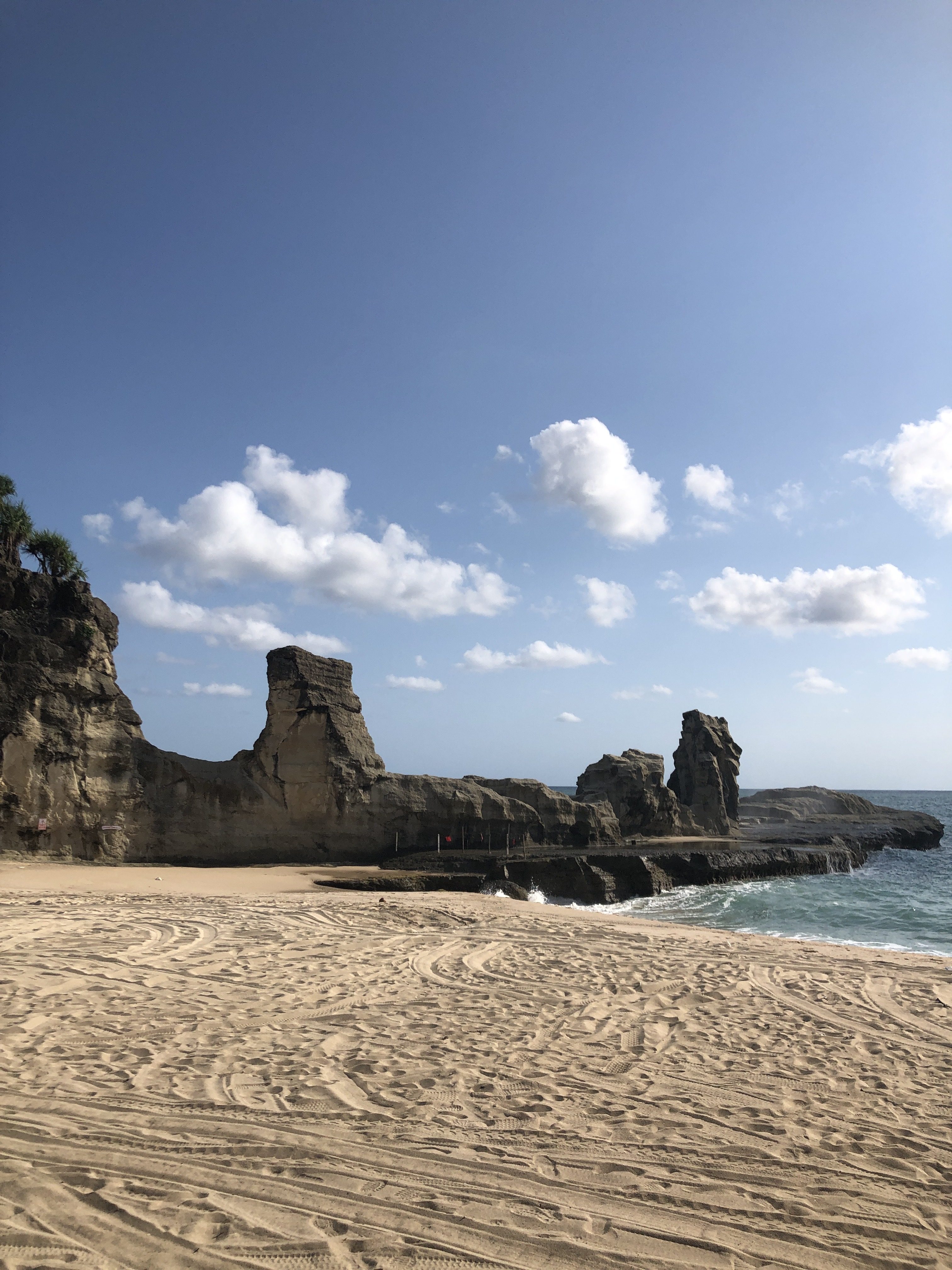 Klayar Beach. Sand in the foreground covered with vehicle tracks, water carved stone formations in the background.