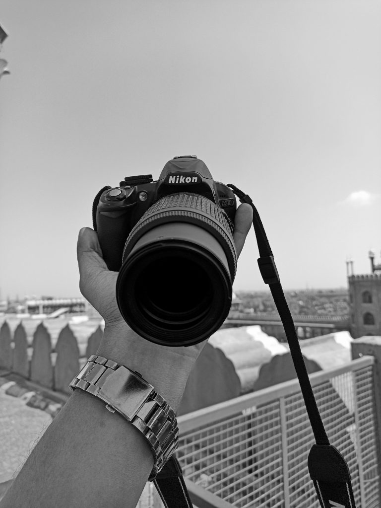 A Nikon camera in the hand of a person. Black & white image.