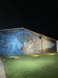 A mural painted on a wall, mostly blue color, of a woman reclining with abstract art behind and around her. 