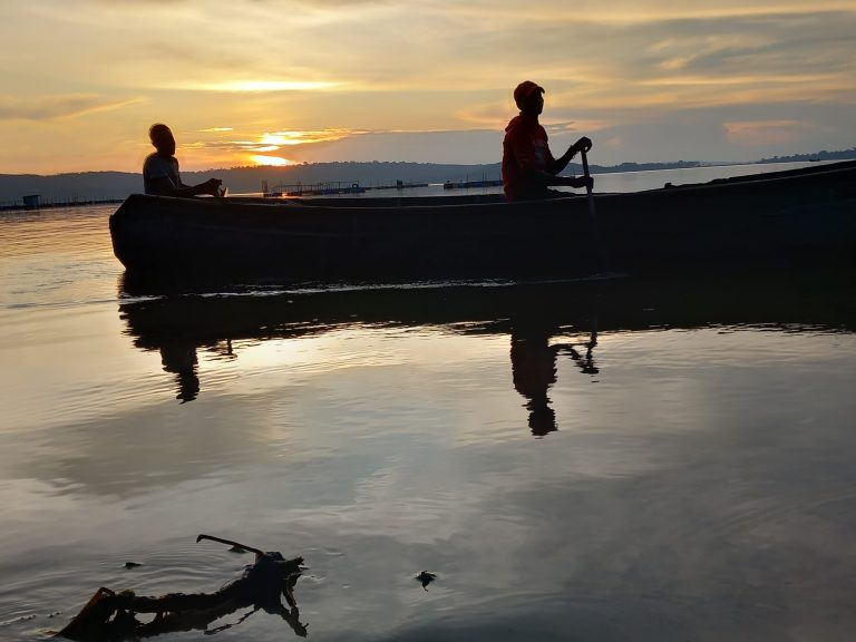 Silhouettes of fisherman rowing a boat, they are reflecting in the water during sunset in the Sesse Islands on Lake Victoria in Uganda  with hills in the distance