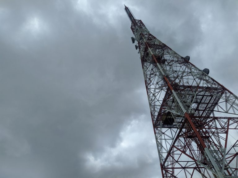 Looking up at a radio tower from its base on a cloudy day