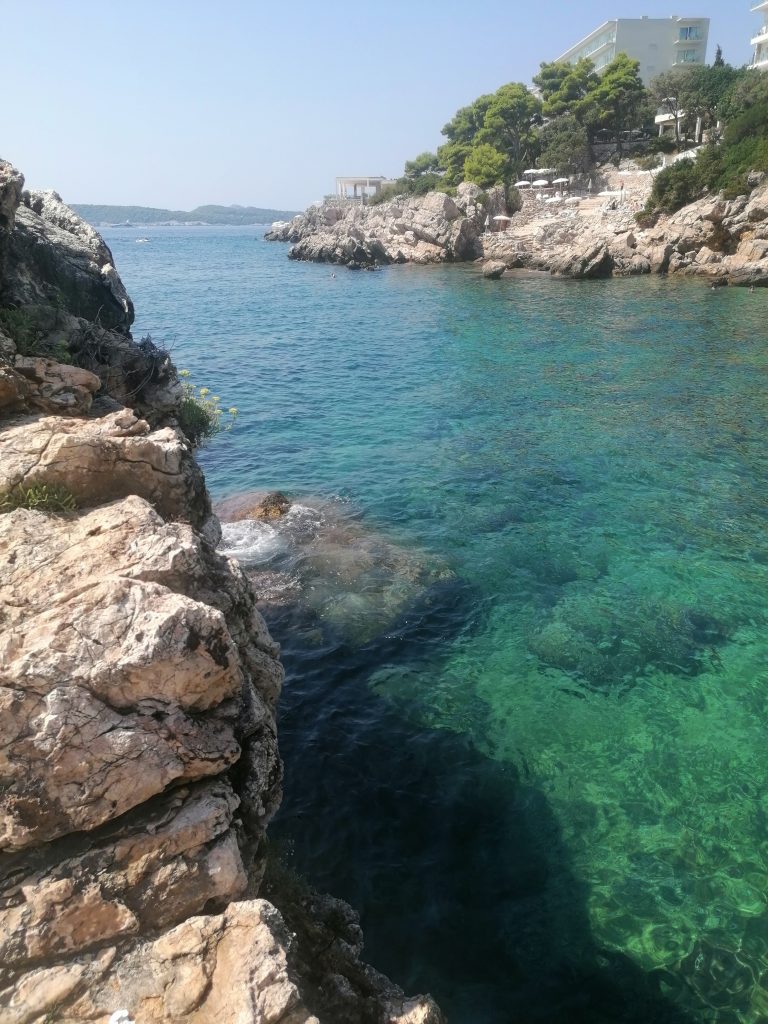 Dubrovnik beach, a water inlet between two rocky outcroppings, where the water is so clear you can see the green bottom.