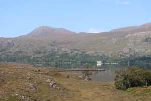 House on the shore of Loch Maree, Scotland on a hazy blue sky day. Torridon Mountains, trees and the house all reflecting into the Loch