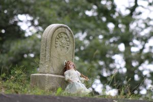 A porcelain doll placed on an old grave marker inscribed “Little Mary”.
